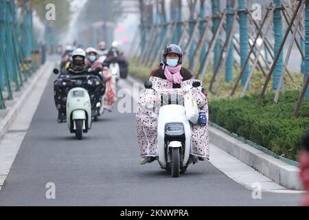 LIANYUNGANG, CHINA - 28. NOVEMBER 2022 - Menschen tragen dicke Winterkleidung und fahren Fahrräder auf einer Straße in Lianyungang, dem östchinesischen Jiangsu Prov Stockfoto