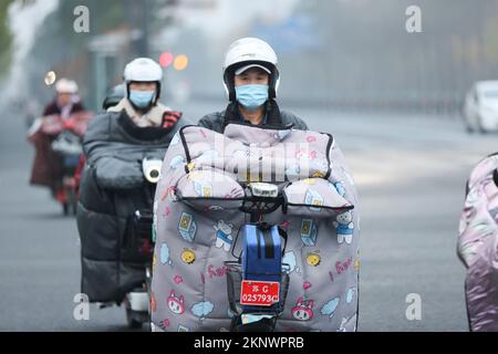 LIANYUNGANG, CHINA - 28. NOVEMBER 2022 - Menschen tragen dicke Winterkleidung und fahren Fahrräder auf einer Straße in Lianyungang, dem östchinesischen Jiangsu Prov Stockfoto