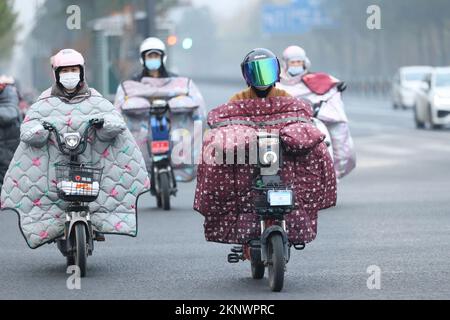 LIANYUNGANG, CHINA - 28. NOVEMBER 2022 - Menschen tragen dicke Winterkleidung und fahren Fahrräder auf einer Straße in Lianyungang, dem östchinesischen Jiangsu Prov Stockfoto