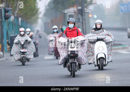 LIANYUNGANG, CHINA - 28. NOVEMBER 2022 - Menschen tragen dicke Winterkleidung und fahren Fahrräder auf einer Straße in Lianyungang, dem östchinesischen Jiangsu Prov Stockfoto