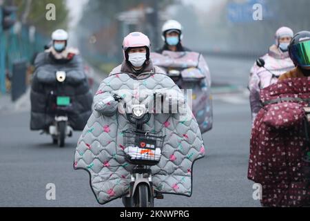 LIANYUNGANG, CHINA - 28. NOVEMBER 2022 - Menschen tragen dicke Winterkleidung und fahren Fahrräder auf einer Straße in Lianyungang, dem östchinesischen Jiangsu Prov Stockfoto