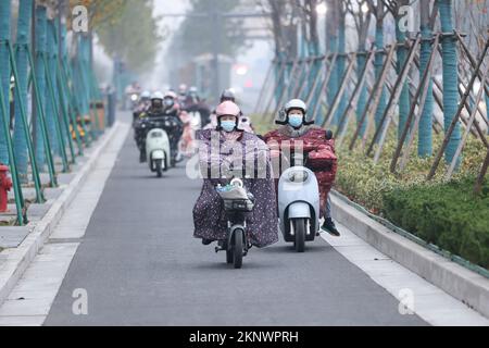 LIANYUNGANG, CHINA - 28. NOVEMBER 2022 - Menschen tragen dicke Winterkleidung und fahren Fahrräder auf einer Straße in Lianyungang, dem östchinesischen Jiangsu Prov Stockfoto