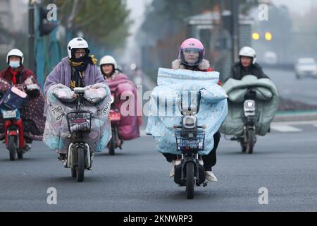 LIANYUNGANG, CHINA - 28. NOVEMBER 2022 - Menschen tragen dicke Winterkleidung und fahren Fahrräder auf einer Straße in Lianyungang, dem östchinesischen Jiangsu Prov Stockfoto