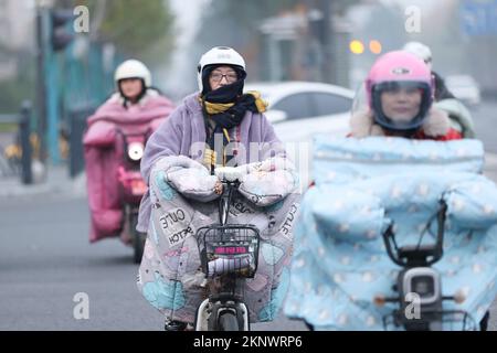 LIANYUNGANG, CHINA - 28. NOVEMBER 2022 - Menschen tragen dicke Winterkleidung und fahren Fahrräder auf einer Straße in Lianyungang, dem östchinesischen Jiangsu Prov Stockfoto