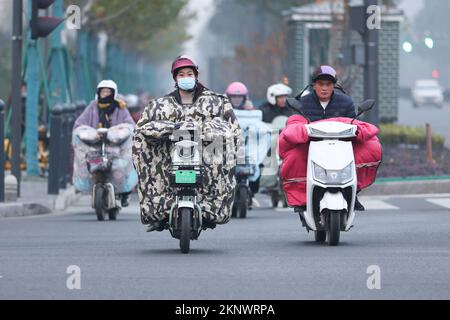 LIANYUNGANG, CHINA - 28. NOVEMBER 2022 - Menschen tragen dicke Winterkleidung und fahren Fahrräder auf einer Straße in Lianyungang, dem östchinesischen Jiangsu Prov Stockfoto