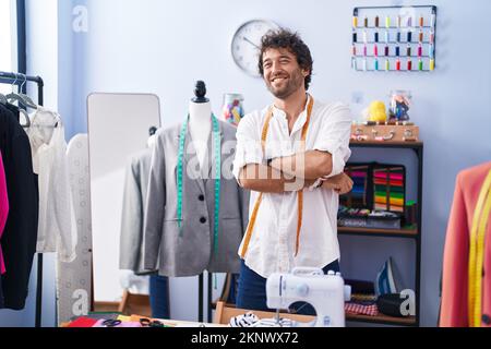 Junger hispanischer Mann, der lächelnd lächelte, stand mit gekreuzten Armen in der Bekleidungsfabrik Stockfoto