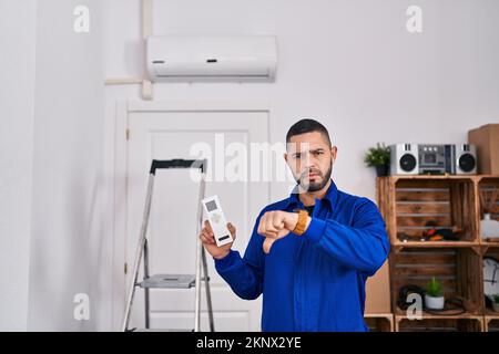 Hispanischer Mechaniker, der mit Klimaanlage arbeitet, mit wütendem Gesicht, negativem Zeichen mit Daumen nach unten, Ablehnungskonzept Stockfoto