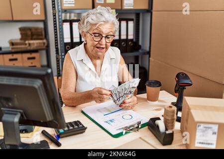 Ältere grauhaarige Geschäftsarbeiterin, die im Büro Dollar zählt Stockfoto