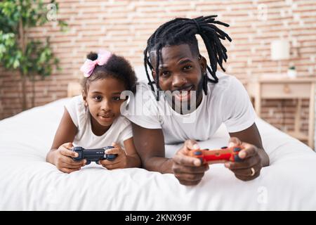 Vater und Tochter spielen Videospiel und liegen im Bett im Schlafzimmer Stockfoto