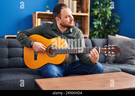 Junger hispanischer Mann spielt klassische Gitarre und sitzt zu Hause auf dem Bett Stockfoto