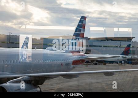 Abstrakte Reflexionen beinhalten das Heck eines Flugzeugs der Alaska Airlines, da die Flugzeuge der American Airlines und der Delta Airlines an Terminal 2, Gates i, beladen werden Stockfoto