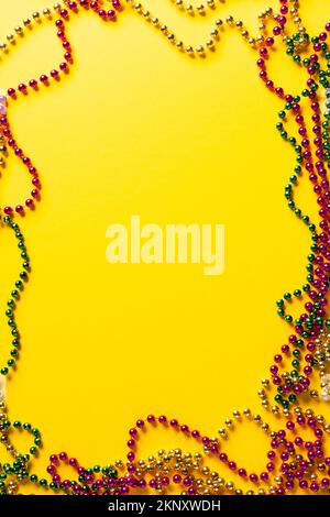 Zusammensetzung von farbigen mardi Gras-Perlen auf gelbem Hintergrund mit zentralem Kopierraum Stockfoto