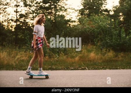 Junge blonde Frau Hipster auf einem Skateboard im Freien bei Sonnenuntergang Stockfoto