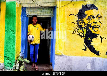 Kalkutta, Indien. 26.. November 2022. Ein Mann posiert mit einem Ball neben einem Wandgemälde, das der Feier der FIFA-Weltmeisterschaft 2022 in Kalkutta gewidmet ist. Kredit: SOPA Images Limited/Alamy Live News Stockfoto