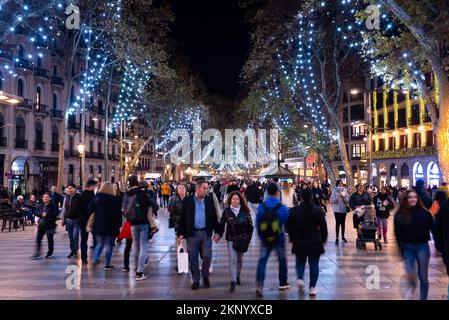 Barcelona, Spanien. 26.. November 2022. Die Menschen laufen nachts unter den Weihnachtslichtern in den beliebten Straßen der „Las Ramblas“ in der Innenstadt. Die Stadtverwaltung von Barcelona hat die Anzahl der Lichter und die Beleuchtungszeiten aufgrund der durch den Krieg zwischen Russland und der Ukraine verursachten erhöhten Energiekosten reduziert. Kredit: SOPA Images Limited/Alamy Live News Stockfoto