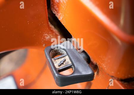 Der Hebel des Luftansaugkabels zum Kaltstart des Motors am Gehäuse einer orangefarbenen Motorsäge in Nahaufnahme. Choke-Taster für fettes Kraftstoffgemisch für Motor Stockfoto