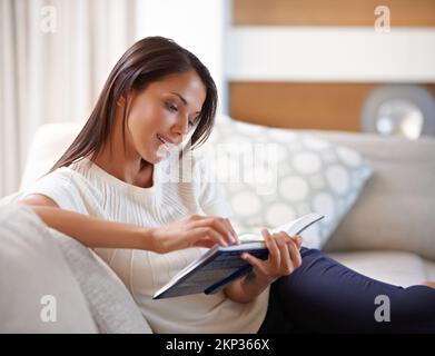 Meine Vorstellung von einem gemütlichen Tag... eine attraktive junge Frau, die zu Hause ein Buch liest. Stockfoto