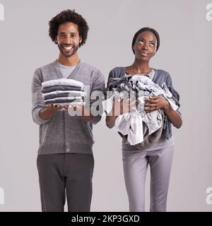 Das erste Mal ist Glück. Studiofoto eines Mannes, der einen ordentlich gefalteten Haufen Kleider hält, während seine Partner in der Klemme stecken. Stockfoto