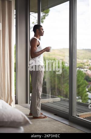 Es gibt nichts Schöneres als eine frische Tasse Kaffee, um Sie auf dem Weg zur Entspannung zu bringen. Ein gutaussehender Mann, der beim Kaffeetrinken aus dem Fenster schaut. Stockfoto