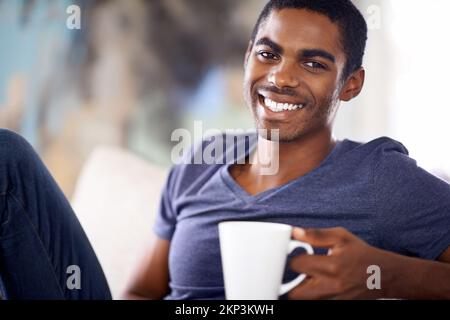 Es gibt nichts Schöneres als eine frische Tasse Kaffee, um Sie auf dem Weg zur Entspannung zu bringen. Ein gutaussehender junger Mann, der sich bei einer Tasse Kaffee entspannt. Stockfoto