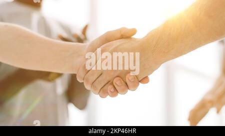 Nahaufnahme. Zwei Kameraden, die sich die Hände schüttelten und in einem Freundeskreis standen Stockfoto