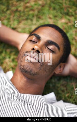 Ein Nickerchen im Freien machen. Ein gutaussehender junger Mann, der draußen auf dem Gras liegt. Stockfoto