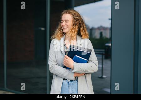 Porträt einer jungen Studentin mit Büchern und Laptop, die nach dem Vortrag von der Universität auf die Straße ging. Menschen und städtischer Lebensstil Stockfoto