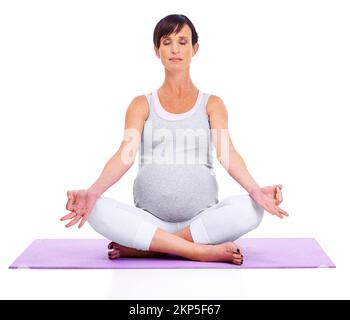 Ruhe und Gelassenheit für Mutter und Baby. Eine junge werdende Mutter meditiert friedlich, während sie auf Weiß isoliert ist. Stockfoto