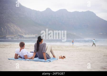 Entspannen am Strand. Rückblick auf ein junges Paar, das am Strand sitzt. Stockfoto