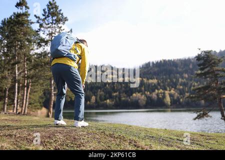 Müder männlicher Reisender mit schwerem Rucksack, der sich in der Nähe des Forest Lake nach hinten bückt Stockfoto