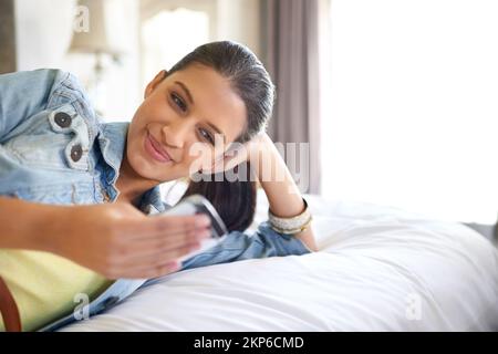 Ich überprüfe ihre Nachrichten. Eine attraktive junge Frau, die sich auf ihrem Bett entspannt. Stockfoto