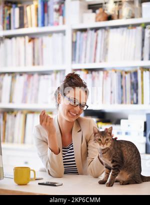 Mein kleiner Furball. Eine attraktive junge Frau, die mit ihrer Katze kuschelt, während sie von zu Hause aus arbeitet. Stockfoto