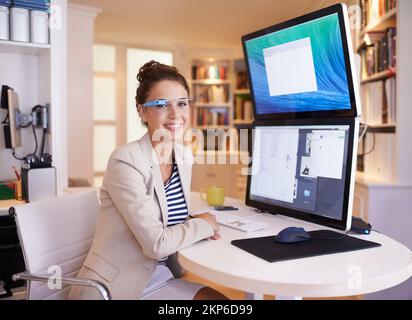 Sie hat die Schönheit und den Verstand hinter ihrem Geschäft. Porträt einer jungen Frau, die eine intelligente Brille trägt, während sie an einem Computer mit zwei Bildschirmen arbeitet. Stockfoto