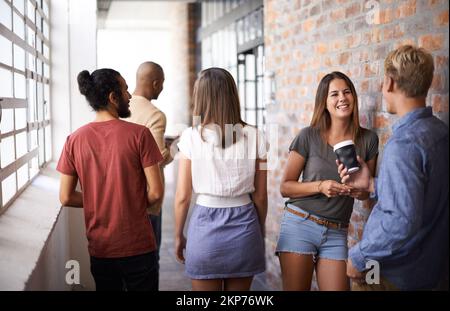 Auf dem Weg zu unserer nächsten Vorlesung. Eine vielfältige Gruppe von Universitätsfreunden, die sich auf dem Flur unterhalten. Stockfoto