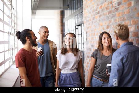 Wir sind auf dem Weg zur nächsten Vorlesung. Eine vielfältige Gruppe von Universitätsfreunden, die sich auf dem Flur unterhalten. Stockfoto