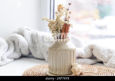 Vase mit getrockneten Blumen und Zimtstäbchen auf verschwommenem Hintergrund. Stockfoto
