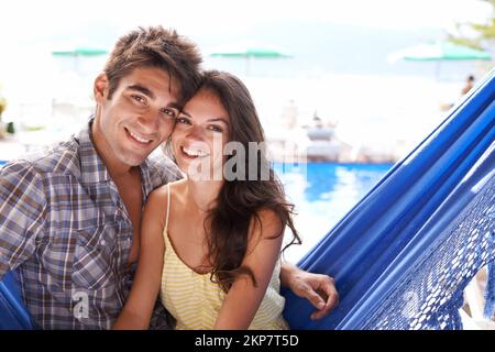 Zusammen im Paradies. Porträt eines liebevollen jungen Paares, das in einer Hängematte sitzt. Stockfoto