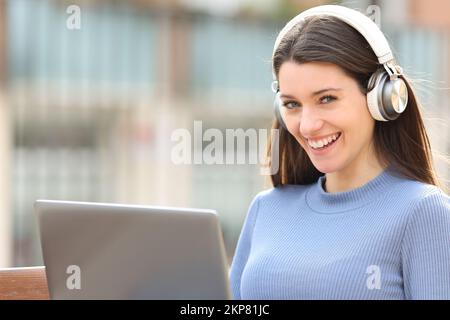 Eine glückliche Frau mit Headset und Laptop sieht Sie auf der Straße an Stockfoto