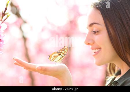 Eine glückliche Frau mit einem Schmetterling in der Hand, die ihn ansieht Stockfoto