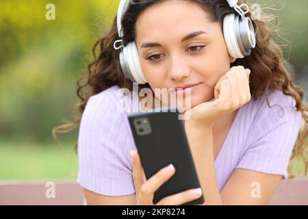 Frau, die mit Kopfhörern Musik hört, in einem Parkprüftelefon Stockfoto