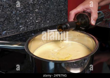 Schwäbische Küche, Zubereitung von Stuttgart-Riesling-Kuchen, Ausgießen von Weißwein aus der Flasche in den Kochtopf, Masse, Auflauf, Induktionskocher, Keramikkochfeld, Stockfoto