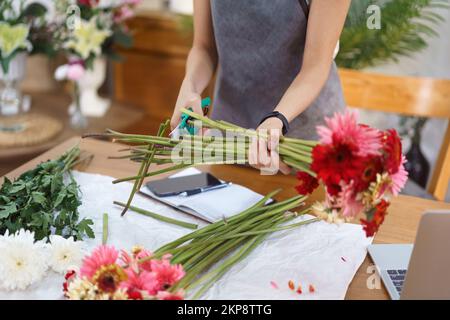 Blumenladen-Konzept, weibliche Floristin schneidet Gerberastiele mit Scheren für Blumensträuße. Stockfoto
