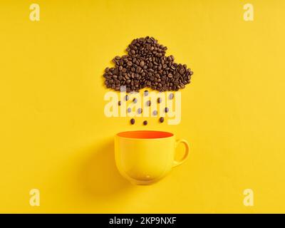 Regnerisches Kaffeekonzept. Kaffeebohnen in Form von Regenwolken und Regentropfen, die auf die Kaffeetasse auf gelbem Hintergrund regnen. Stockfoto