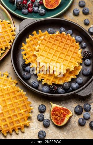 Knusprige Waffeln und Beeren in einer Pfanne. Eine halbe Feige, Blaubeeren und Waffeln. Flach verlegt. Rostiger Metallhintergrund. Stockfoto