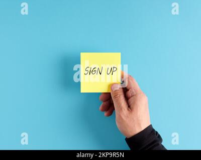 Männliche Hand hält eine gelbe Haftnotiz mit dem Wort "Sign up". Anmelde- und Mitgliedschaftskonzept. Stockfoto