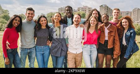 Eine große Gruppe multiethnischer Freunde, die sich draußen umarmen, lächeln und in die Kamera schauen – Vielfalt, Freundschaft, Einheit, Vereinigung und Lebensstil der Menschen Stockfoto