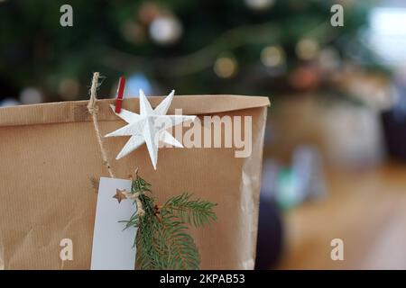 Weihnachtsgeschenkbox aus Recyclingpapier mit weihnachtsbaum im Hintergrund. Stockfoto