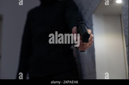 Androhung von Schusswaffen. Der Fang der Waffe in der Hand des Mannes wird auf die Kamera gerichtet. Männlicher Verbrecher hält Revolver auf schwarzem Hintergrund. Angriff oder Verteidigung Stockfoto