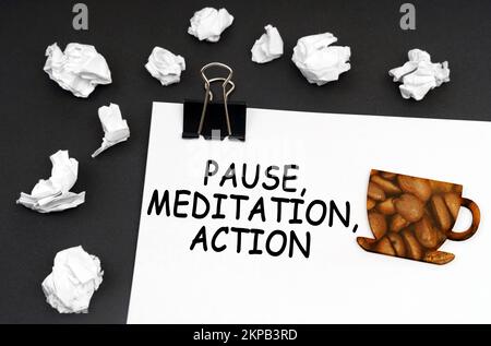 Ruhe bei der Arbeit. Auf der schwarzen Oberfläche befindet sich ein weißes Blatt mit der Aufschrift „Pause Meditation Action“, eine Tasse mit einem Bild von Kaffeebohnen. Stockfoto