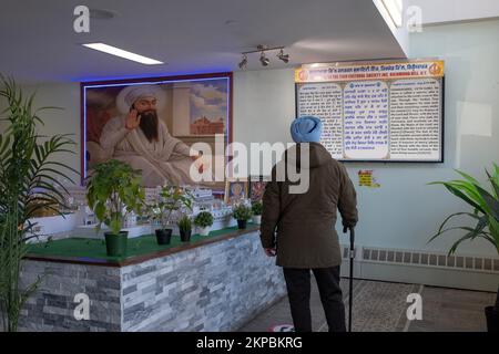 Ein unbekannter älterer Sikh-Mann liest ein dreisprachiges Schild am Eingang zum Sikh Cultural Center in Richmond Hill, Queens, New York City. Stockfoto